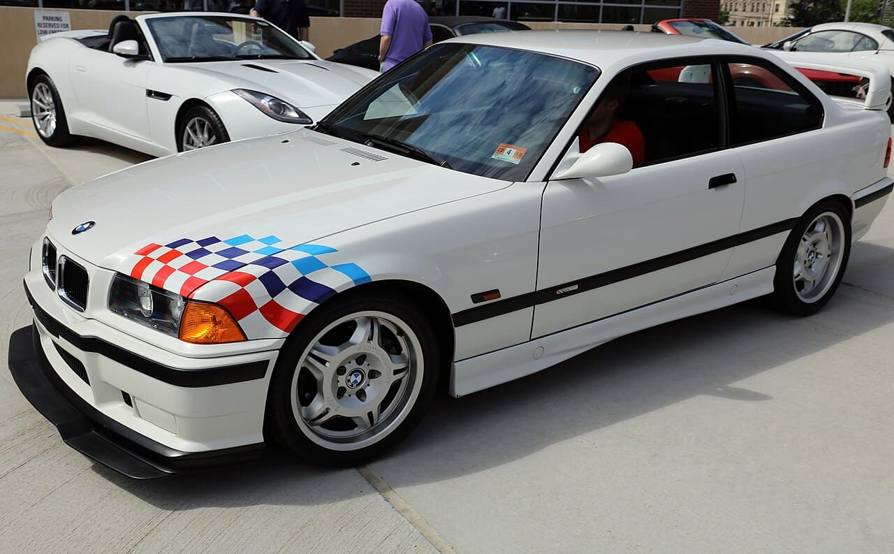 The Alpine White M3 Lightweight with its Motorsport flag graphics, deleted equipment, and aluminium door skins. Wikimedia Commons · Mr.choppers · CC BY-SA 3.0