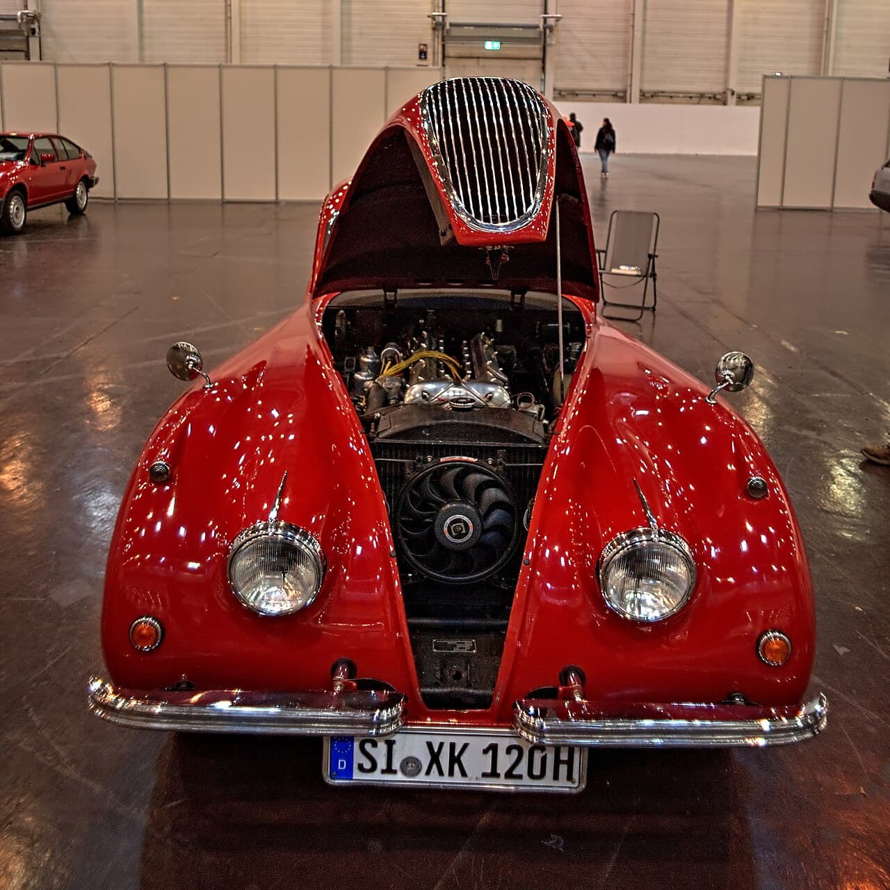 A Jaguar XK120 with its bonnet raised over the XK twin-cam straight-six, the engine behind the Jaguar postwar performance era. Wikimedia Commons · Thomas Vogt · CC BY 2.0